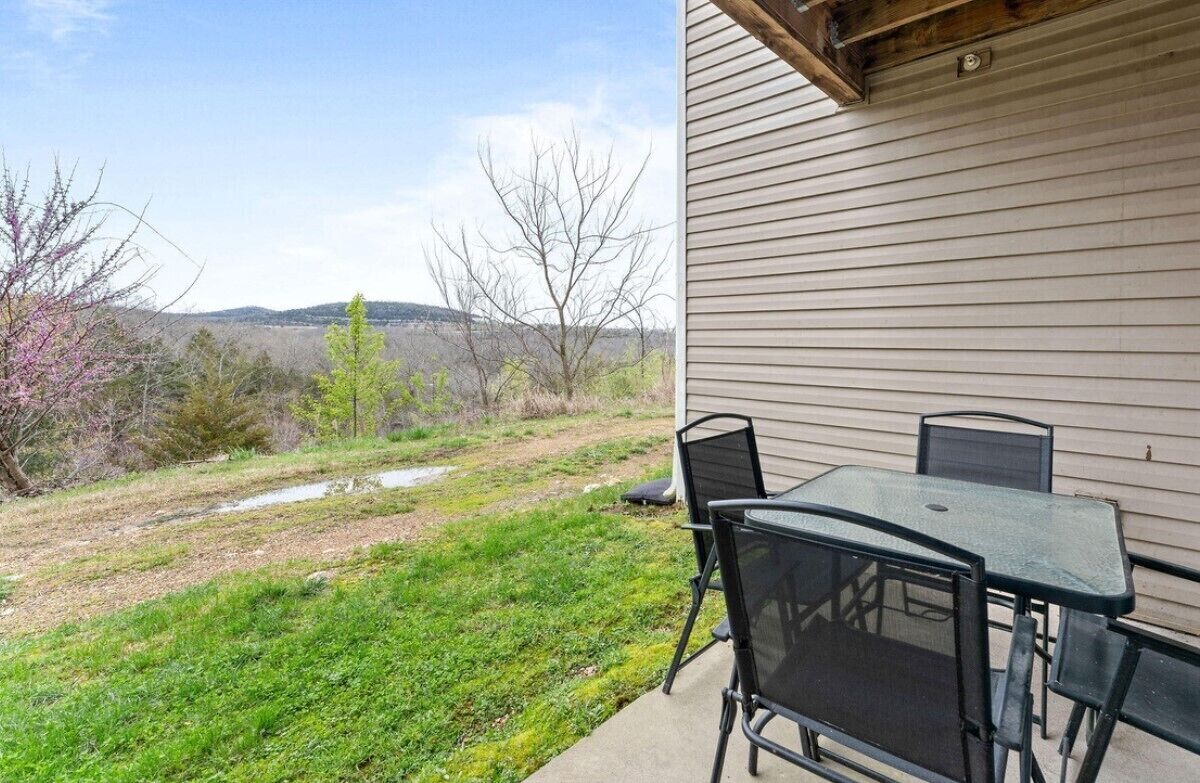 A patio with a table and chairs, a grassy area, and a view of hills in the background.