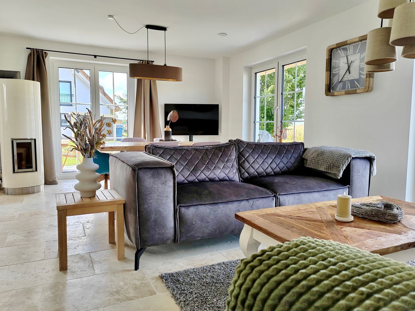 Un salon moderne avec un canapé en cuir foncé, une table basse en bois, un téléviseur et une grande fenêtre avec des rideaux.