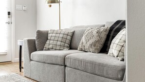 Un sofà gris amb coixins estampats i amb textures, una làmpada de peu i una paret blanca.