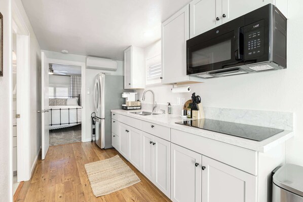 A modern kitchen with white cabinetry, a black microwave, and a stainless steel sink.