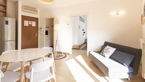 A modern living room with a sofa, a dining table with chairs, a lamp, and a kitchen area with a refrigerator. - Via Marcona 17 Apartment (Milano)