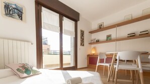 A hotel room with a bed, a desk, chairs, a window with blinds, and a view of the outside. - Via Marcona 17 Apartment (Milano)