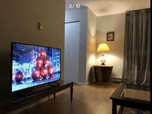 A living room with a flat-screen TV on a stand, a lamp on a side table, and a door in the background. - 2-Storey Entire Home close to Lakehead University (Thunder Bay)