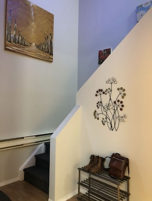 A staircase with a metal rack holding boots and a handbag, a painting on the wall, and a decorative wall piece. - 2-Storey Entire Home close to Lakehead University (Thunder Bay)