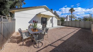 A white single-story house with a covered patio, a gravel driveway, and a wooden fence. - Casa flower centrally located  (Tucson)