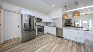 A modern kitchen with white cabinetry, stainless steel appliances, a herringbone-patterned backsplash, and a wooden floor. - Casa flower centrally located  (Tucson)