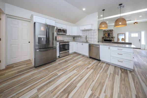 A modern kitchen with white cabinetry, stainless steel appliances, a herringbone-patterned backsplash, and a wooden floor.