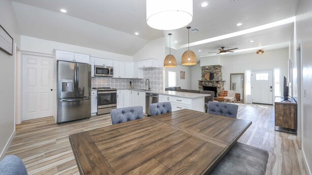A modern kitchen with a large island, stainless steel appliances, and a dining area with a wooden table and cushioned chairs. - Casa flower centrally located  (Tucson)
