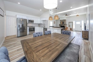 A modern kitchen with a large island, stainless steel appliances, and a dining area with a wooden table and cushioned chairs.