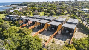 A row of modern, compact cabins with flat roofs, situated in a lush, green landscape with a view of the ocean. - Ingenia Holidays Cape Paterson (Cape Paterson)