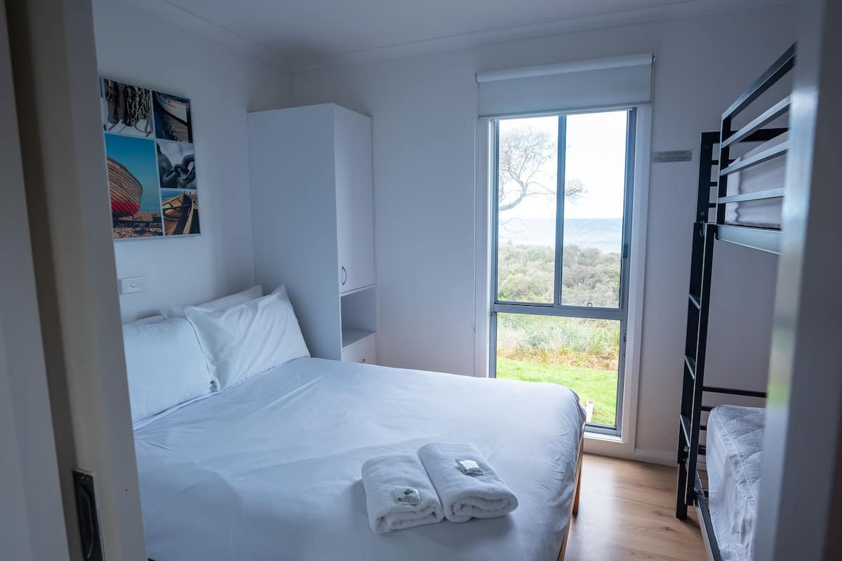 A bedroom with a bed, a window, a bunk bed, and a wall with artwork.
