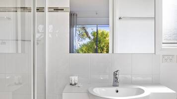 A modern bathroom with a glass shower enclosure, a white sink, and a window with a view of trees.