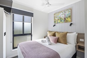 A modern hotel room with a large bed, a ceiling fan, a window with blinds, and a painting on the wall. - Ingenia Holidays Cape Paterson (Cape Paterson)