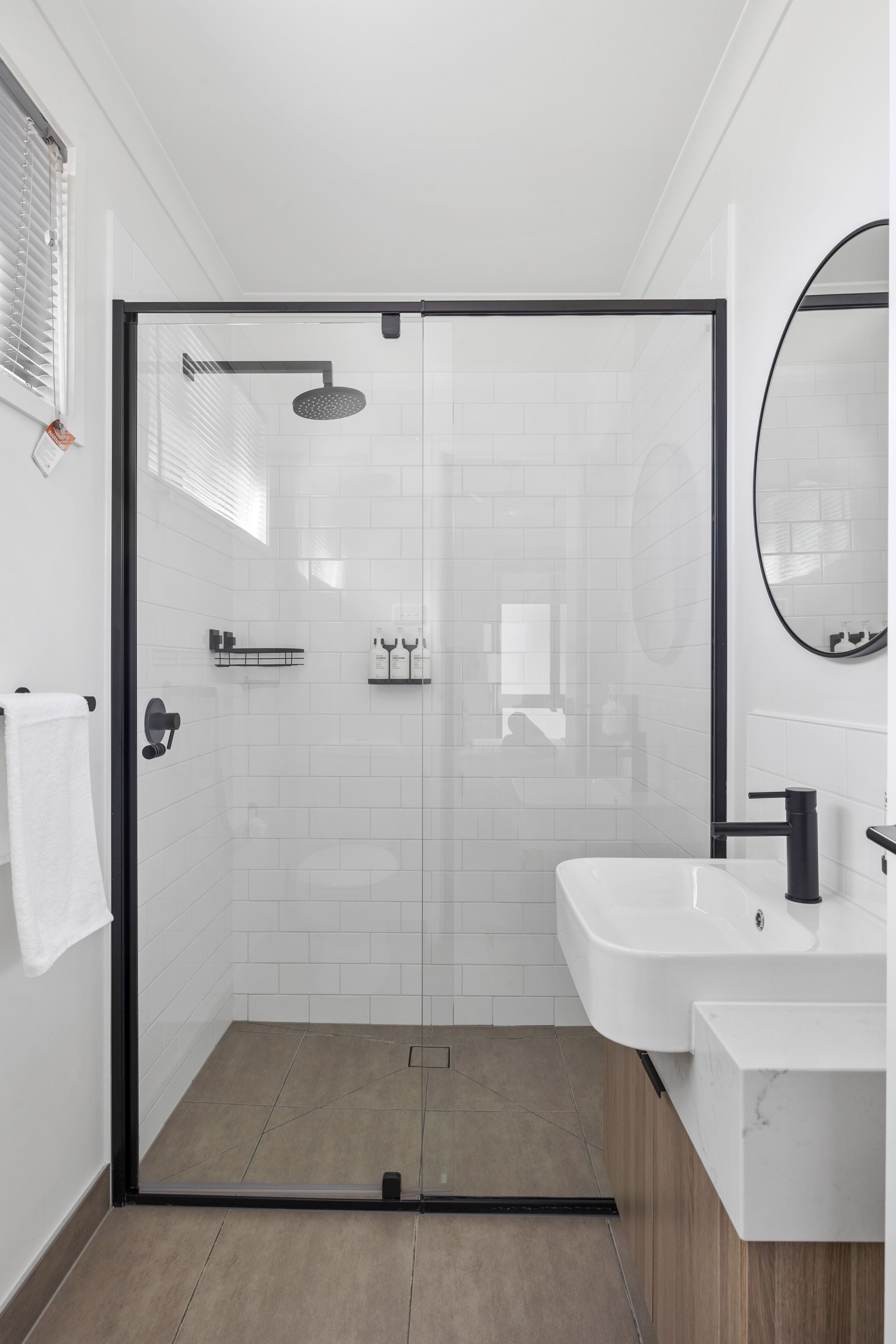 Un baño moderno con ducha de vidrio, azulejos blancos, un lavamanos blanco y un espejo.
