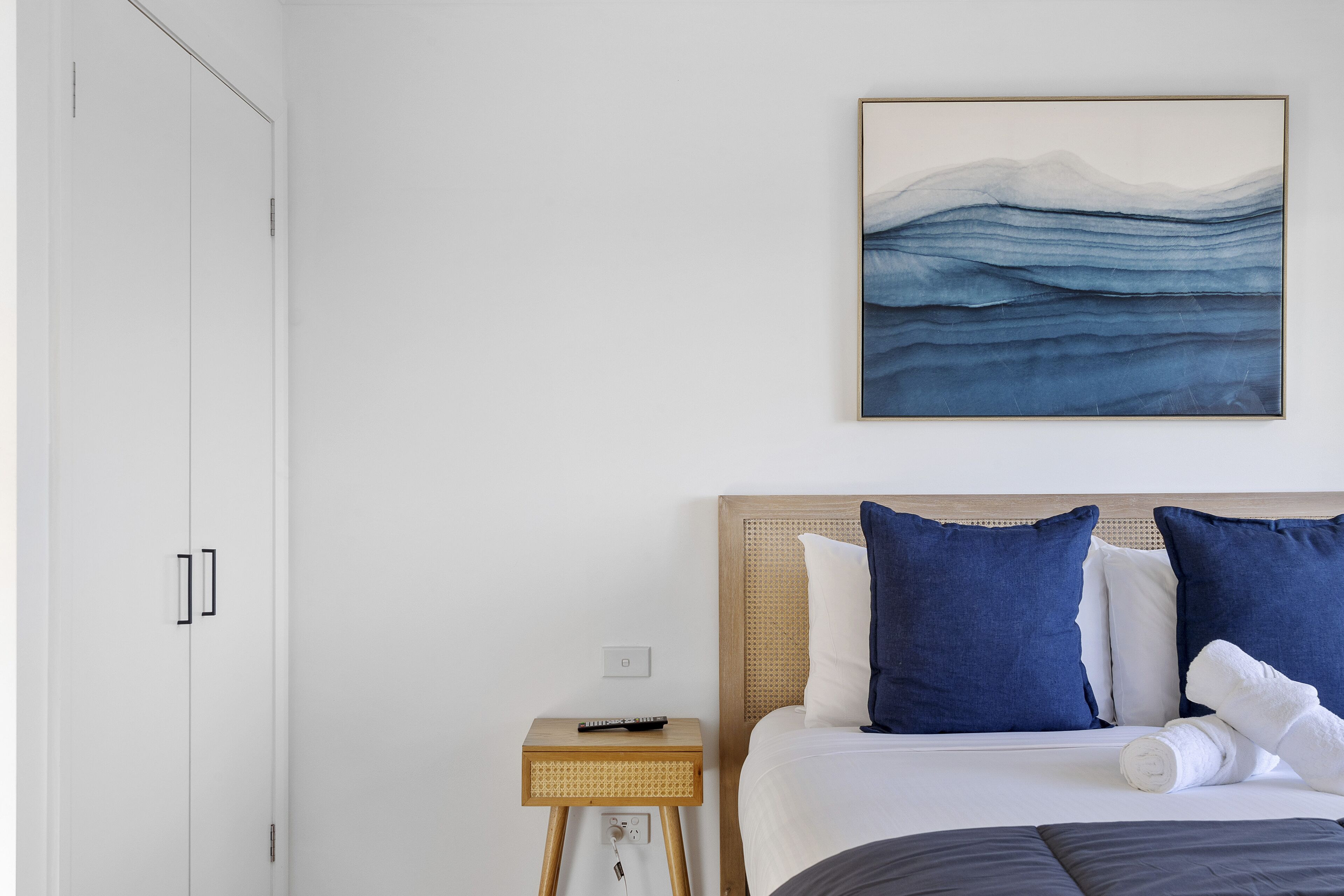 Habitación de hotel con cama, mesita de noche, control remoto y una obra de arte en la pared.
