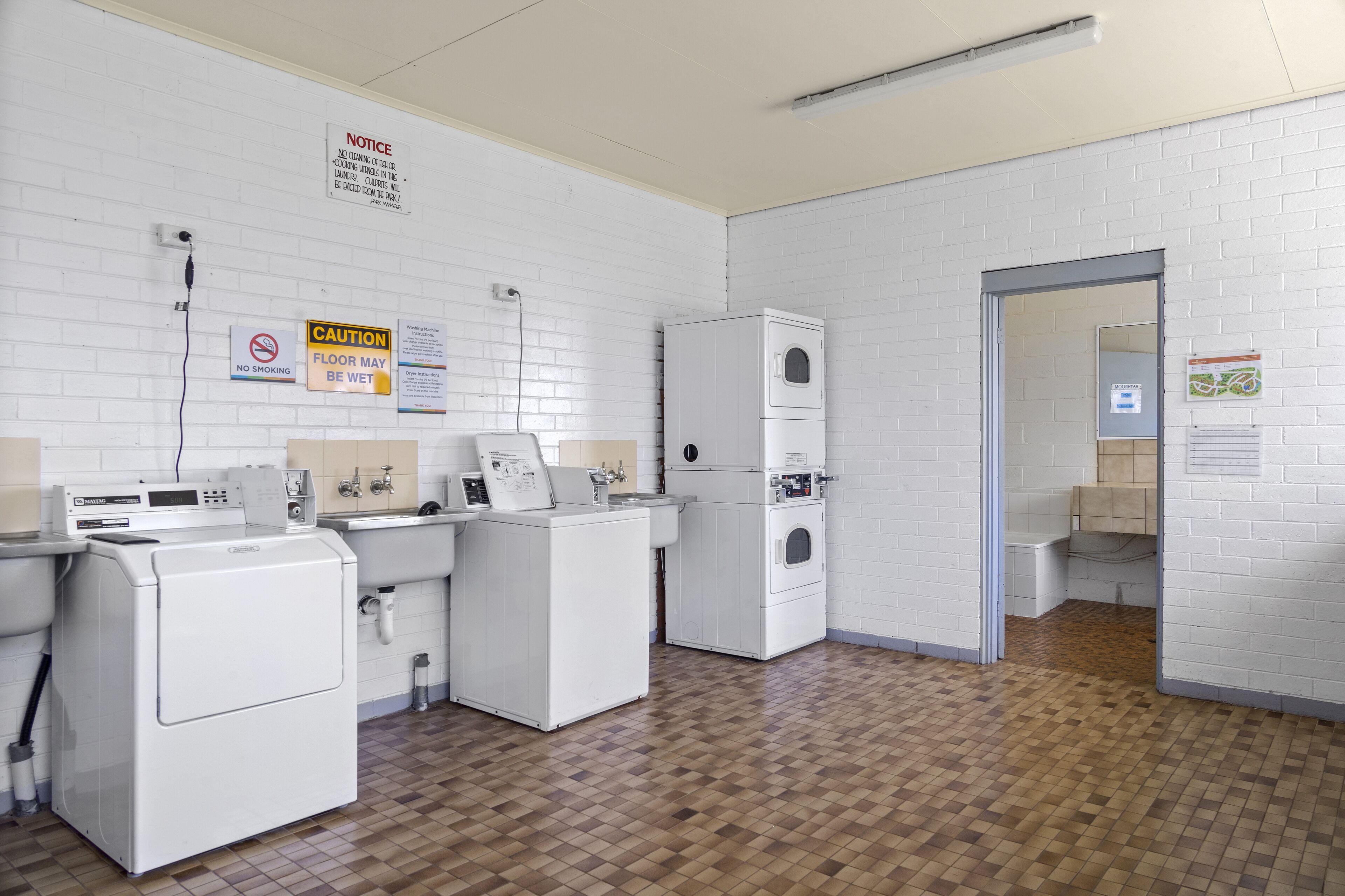 A laundry facility with multiple washing machines and dryers, a no smoking sign, and caution signs.