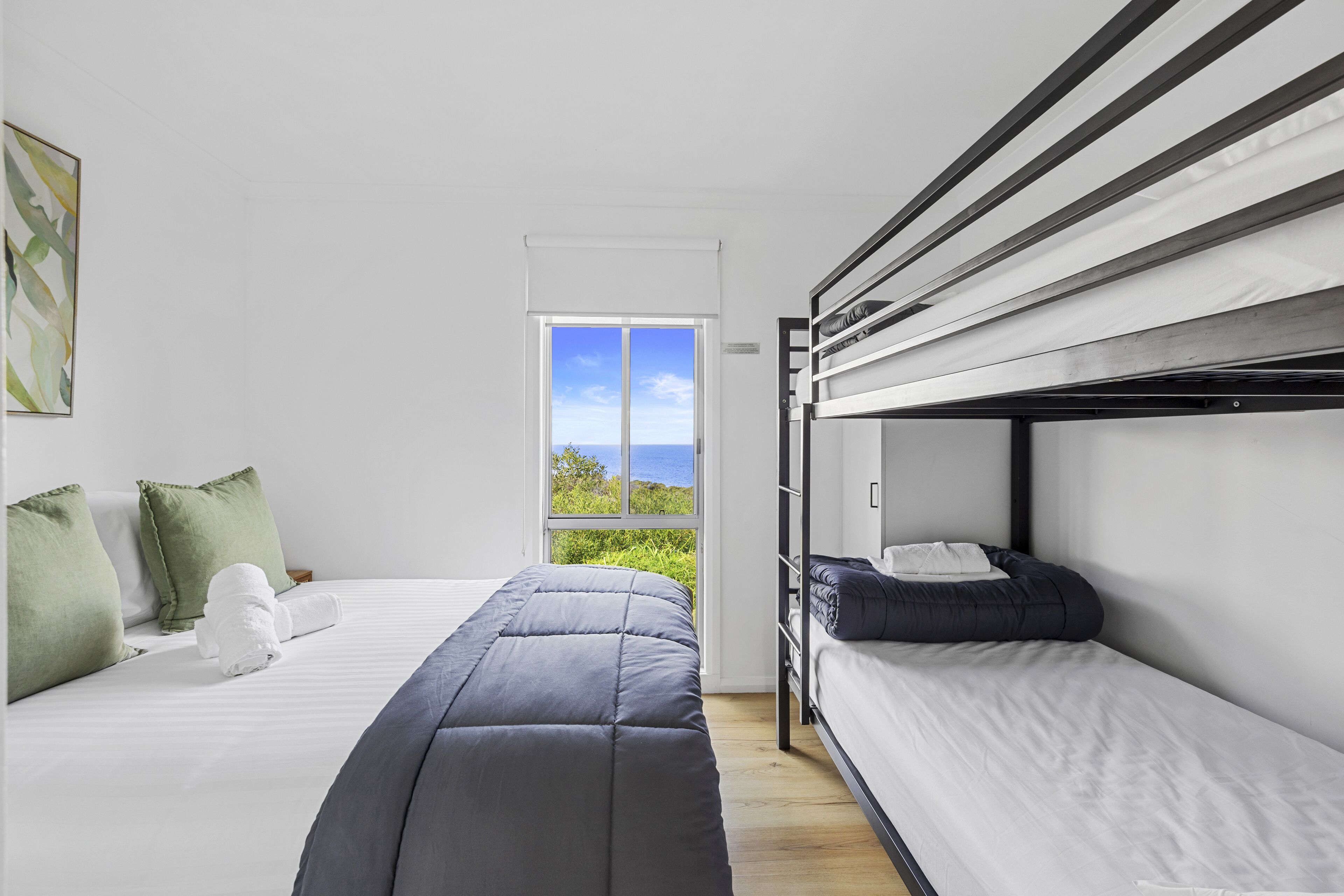 A modern bedroom with a bunk bed, a single bed, and a large window offering a view of the outdoors.