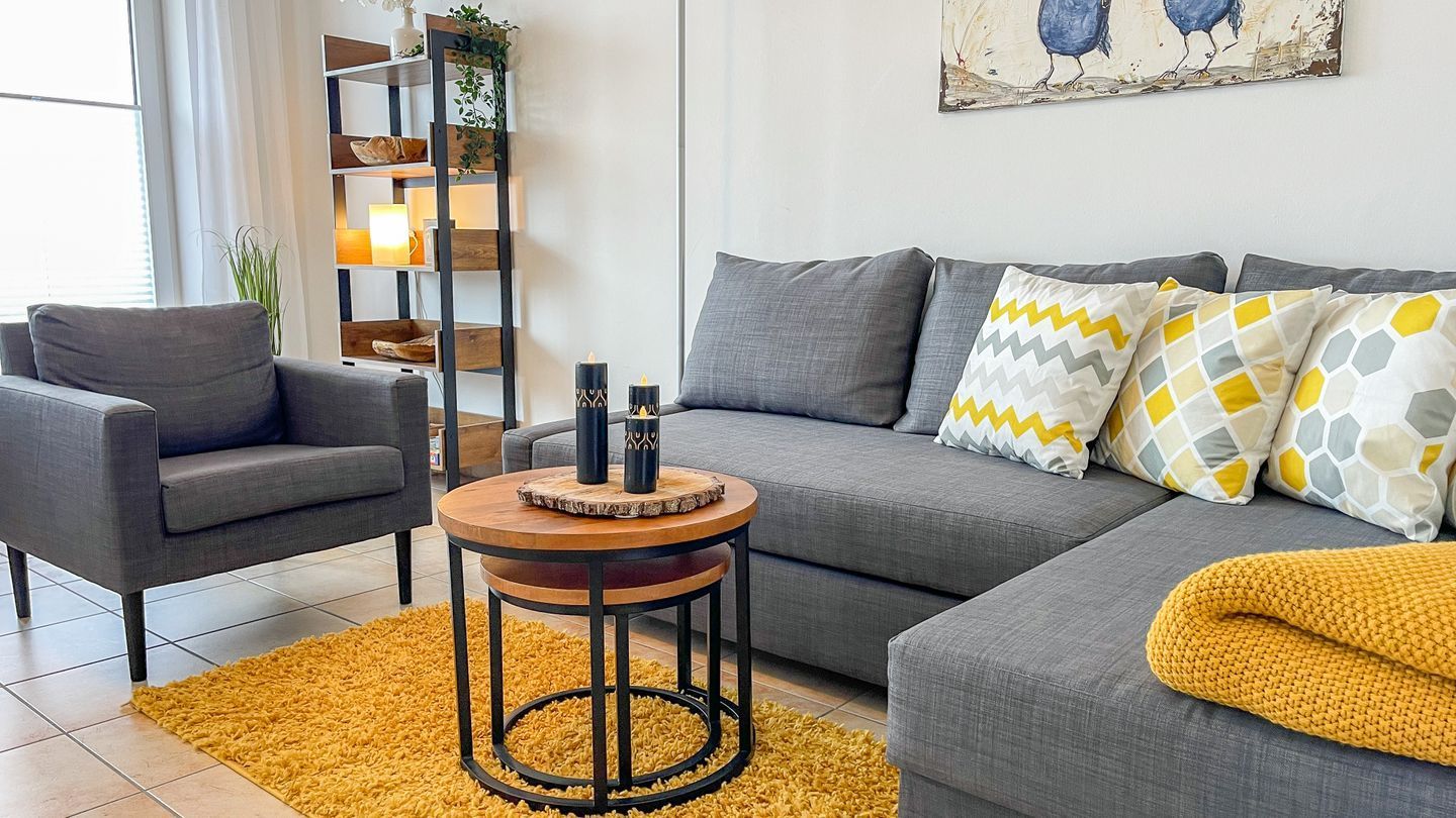 Ein modernes Wohnzimmer mit einem grauen Sofa, einem runden Holztisch und einem gelben Teppich.
