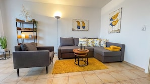 Un salon avec un canapé, un fauteuil et une table basse. On y trouve également un lampadaire et des œuvres d’art accrochées au mur.