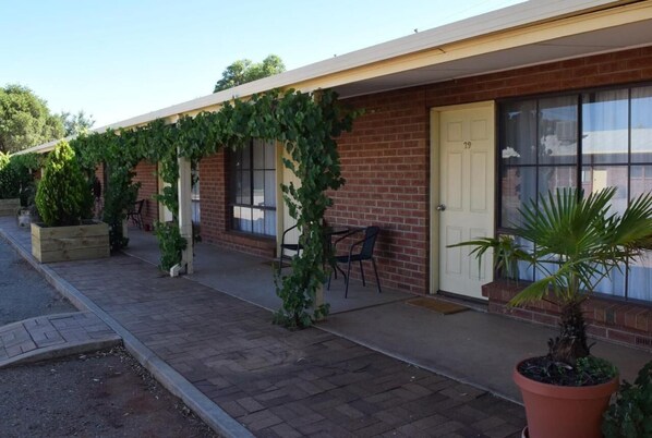 A building with a brick facade, a covered porch with chairs, and potted plants.
