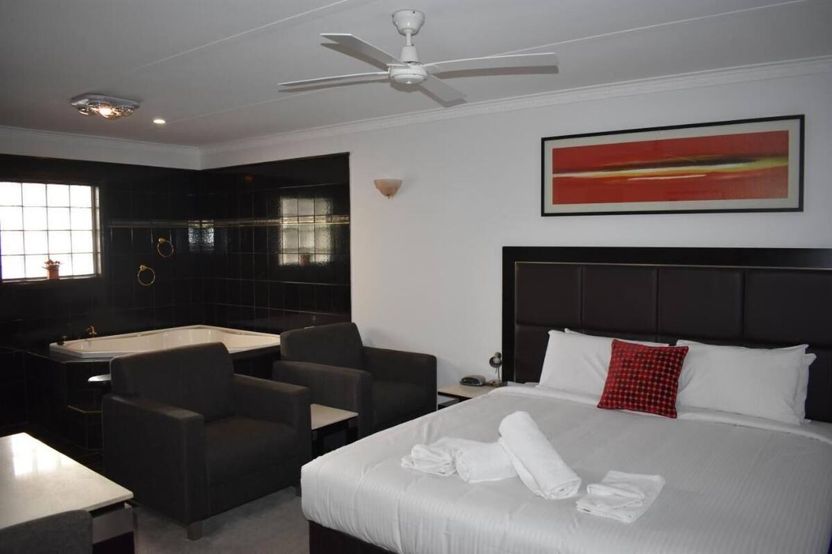 A hotel room with a bed, a sitting area with chairs, a bathtub, and a ceiling fan.