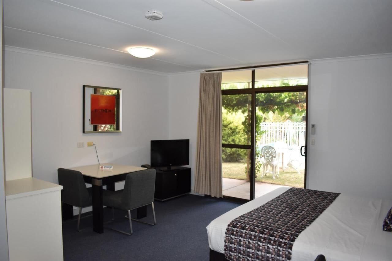 A hotel room with a bed, a desk with a chair, a television, and a sliding glass door leading to an outdoor area.