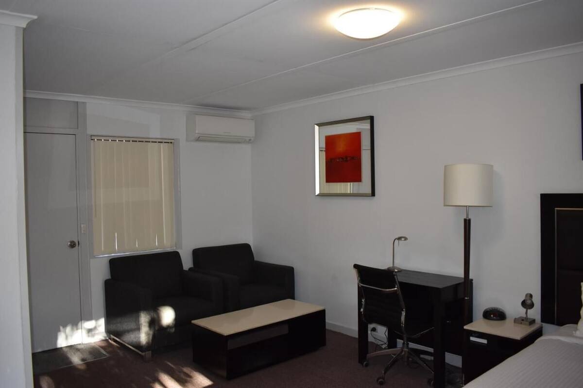A hotel room with a black sofa, a small desk, a lamp, and a bed.