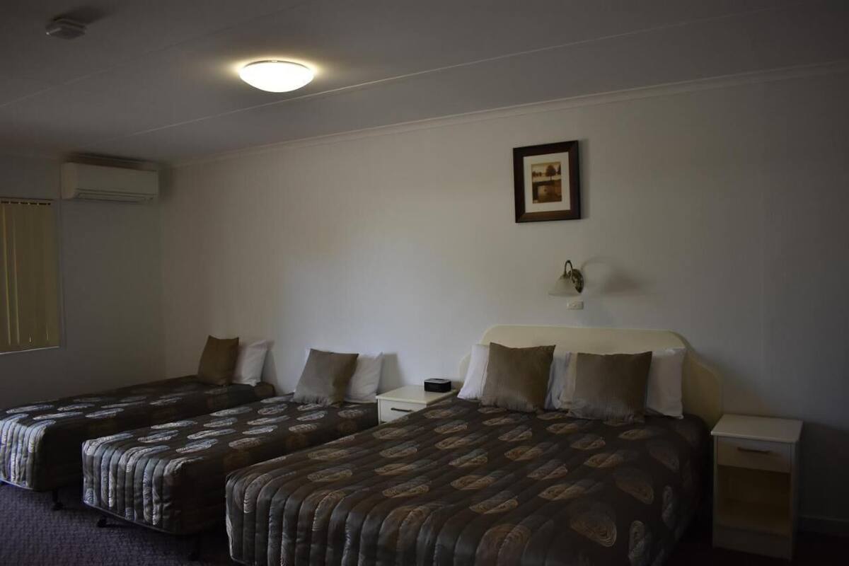 A hotel room with two beds, a bedside table, a nightstand, a framed picture on the wall, and an air conditioning unit.