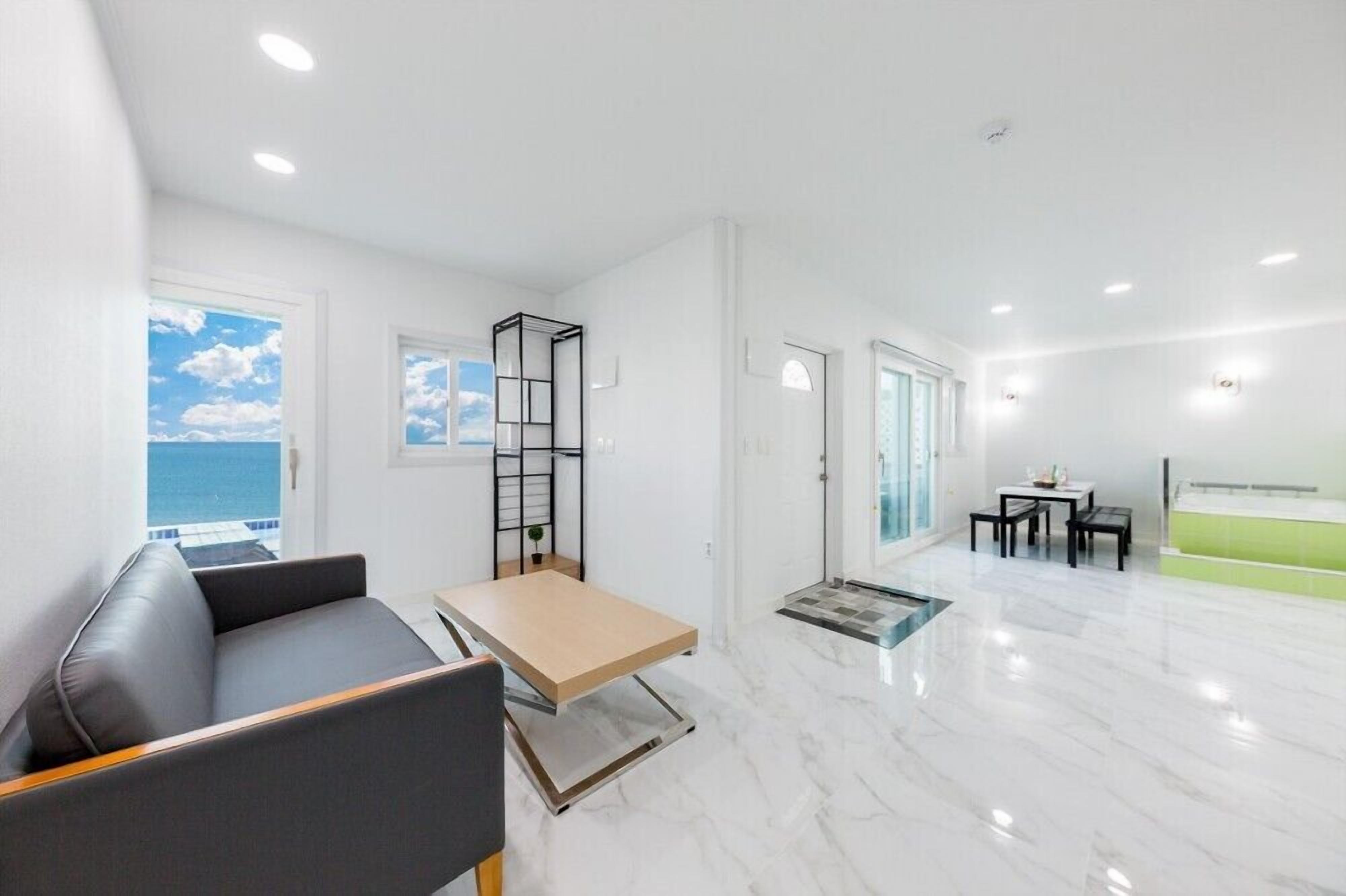 A modern living room with a sofa, a small table, and a view of the sea through large windows.