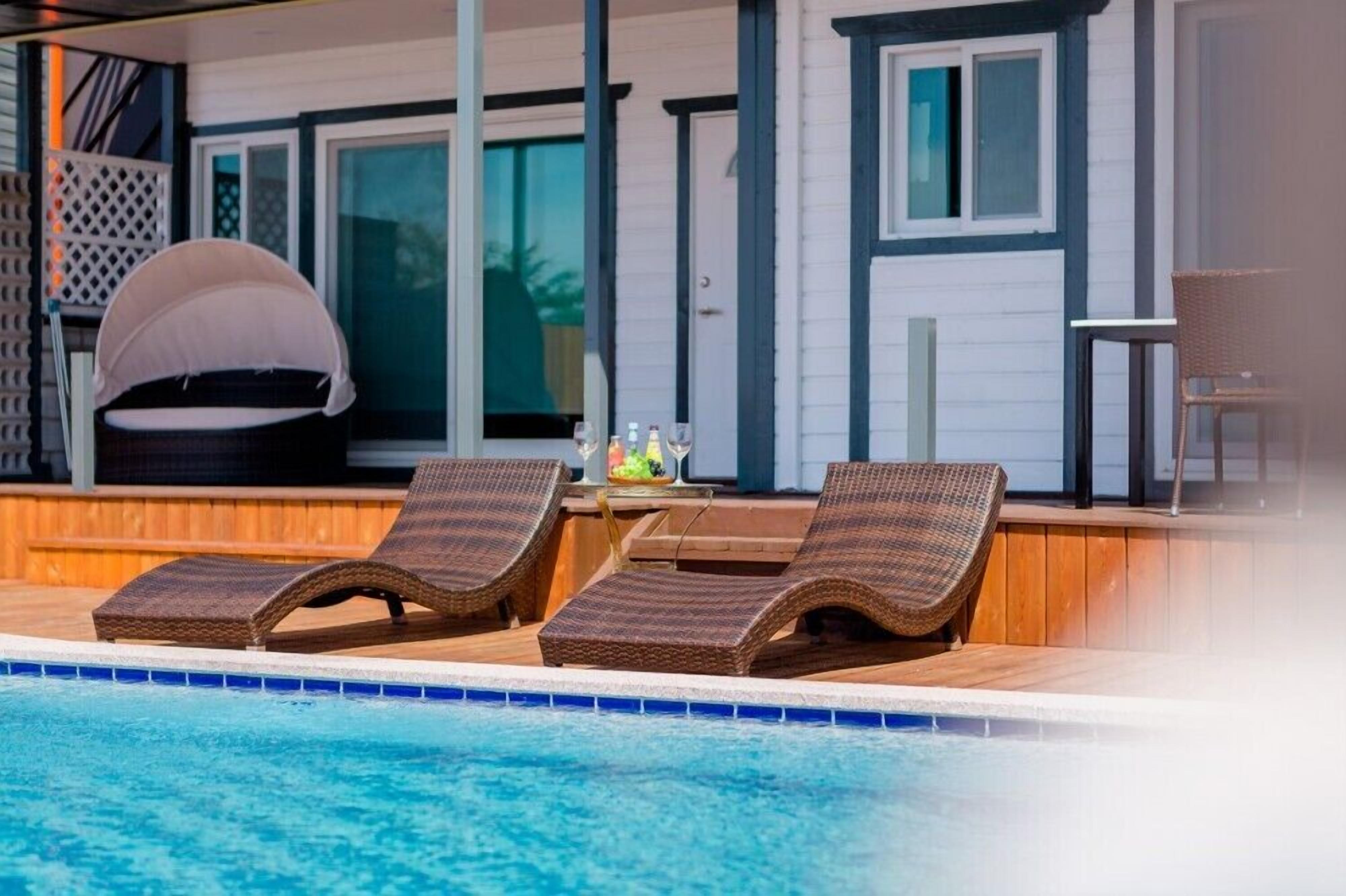 A poolside area with lounge chairs, a covered seating area, and a table with drinks.
