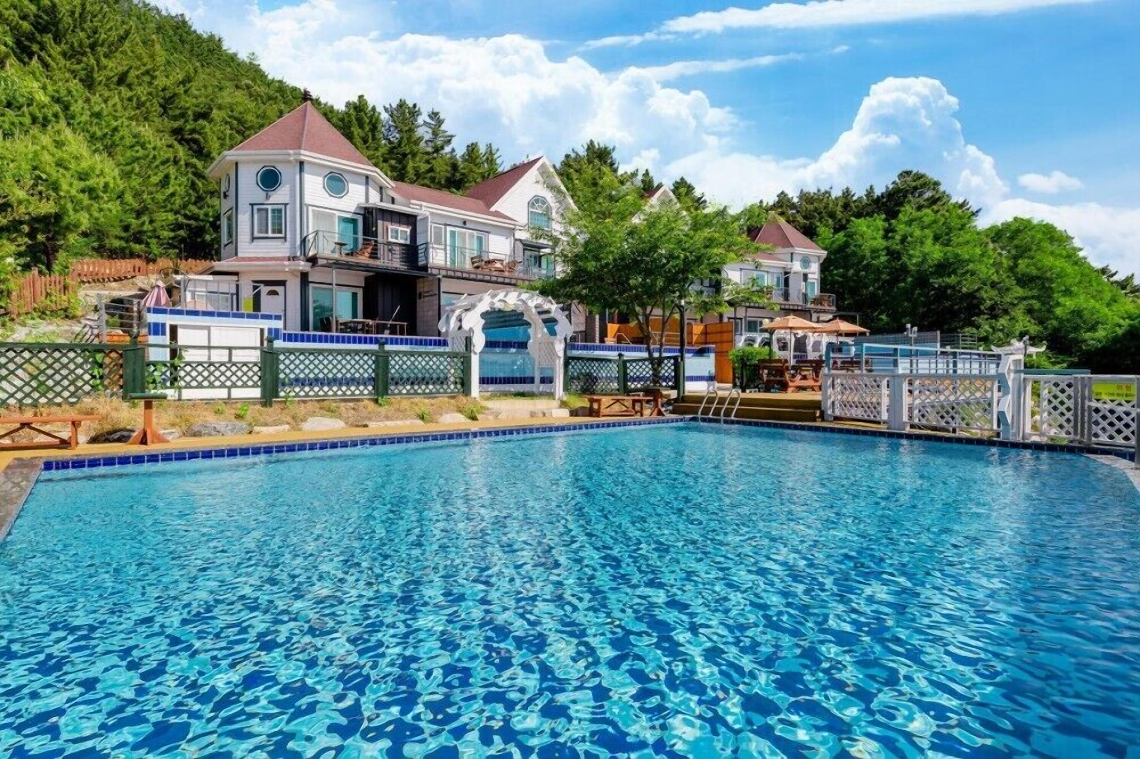 A swimming pool with a tiled deck and a house in the background.