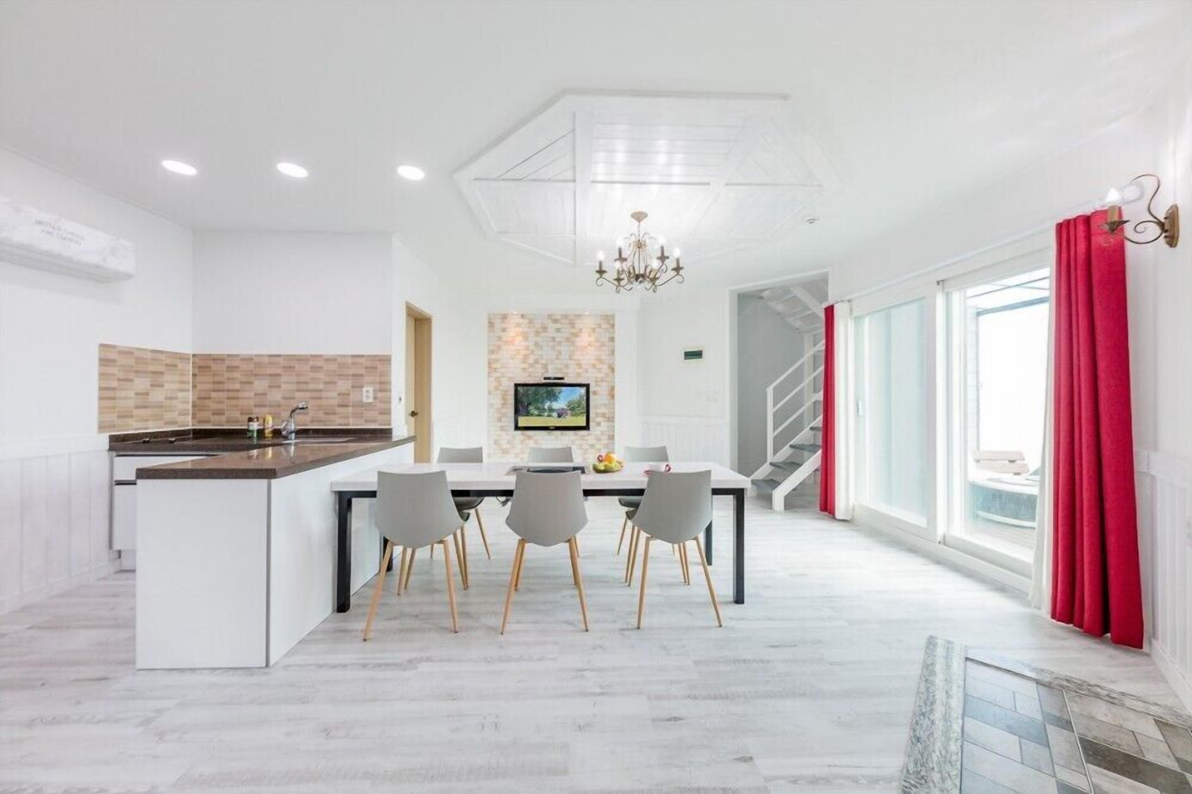 A modern kitchen with a central island, a dining area with chairs, a TV mounted on the wall, and a staircase leading to another level.
