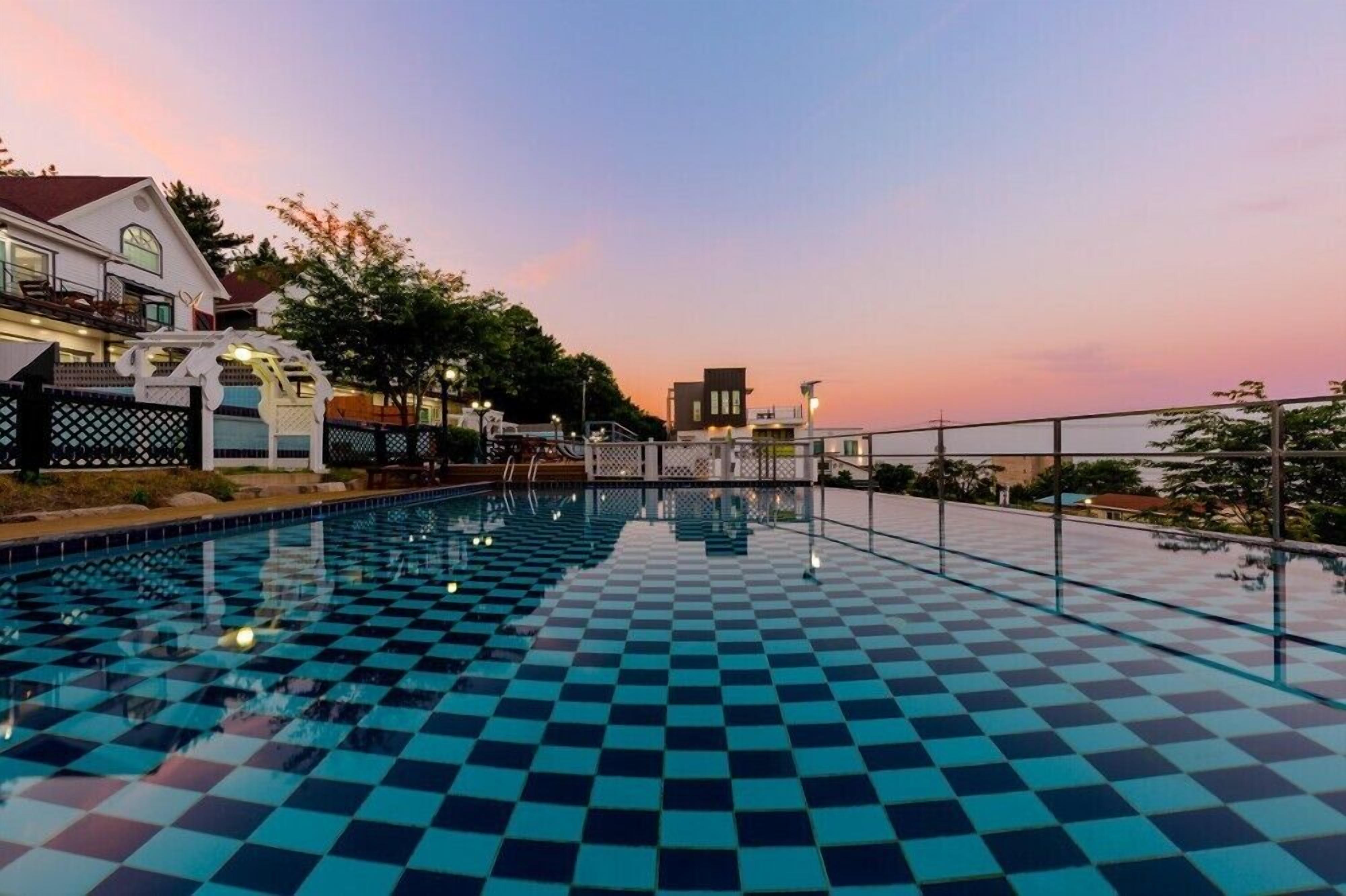 A swimming pool with a checkered pattern, surrounded by a fence and trees.