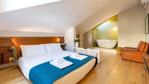 Una habitación de hotel moderna con una cama grande, un baño con bañera y una zona de estar acogedora.
