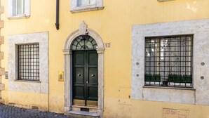 Un edificio amarillo con puerta verde, una ventana con rejas y un letrero con el número 12.