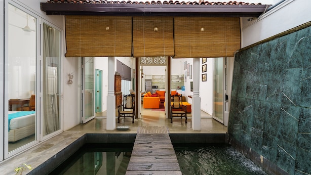 Ein modernes Interieur mit Pool, einer Holzterrasse und Blick in einen Wohnbereich mit orangefarbenen Möbeln.