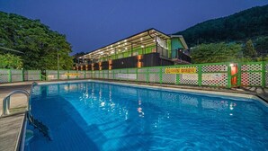 Ein Pool mit Holzterrasse, umgeben von einem grünen Zaun mit weißen Gitterelementen.
