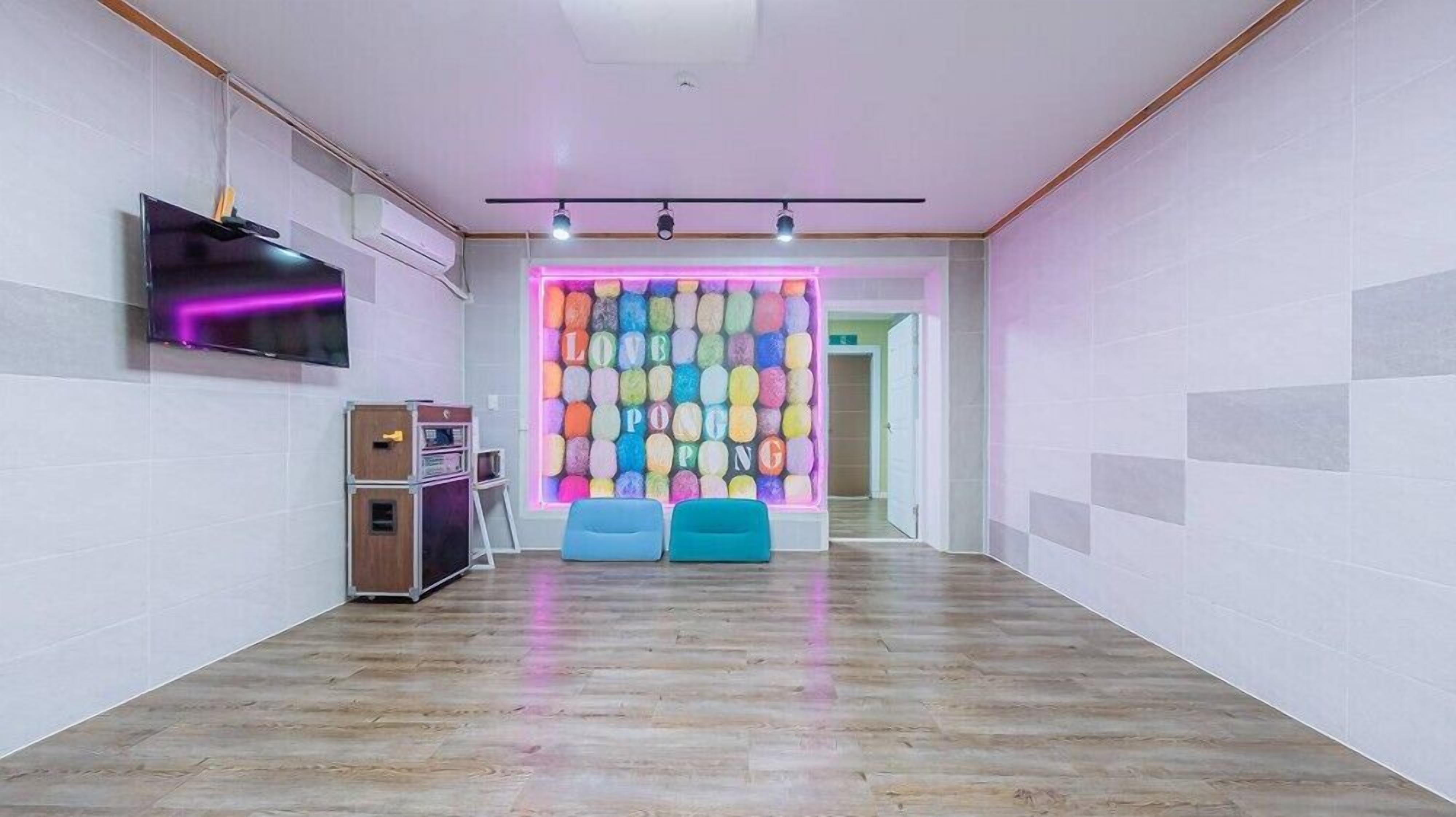 A modern room with a wooden floor, a wall-mounted TV, a colorful wall decoration, and two blue chairs.