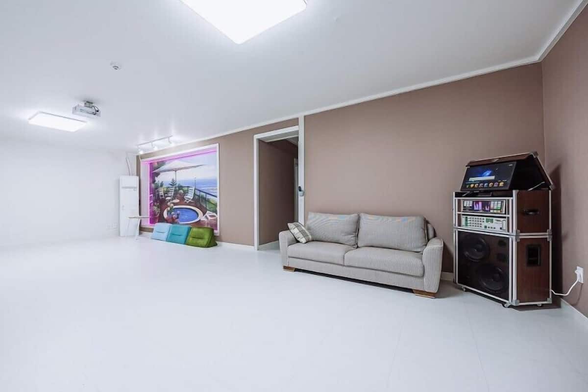 A spacious room with a large window, a sofa, a sound system, and a colorful mural.