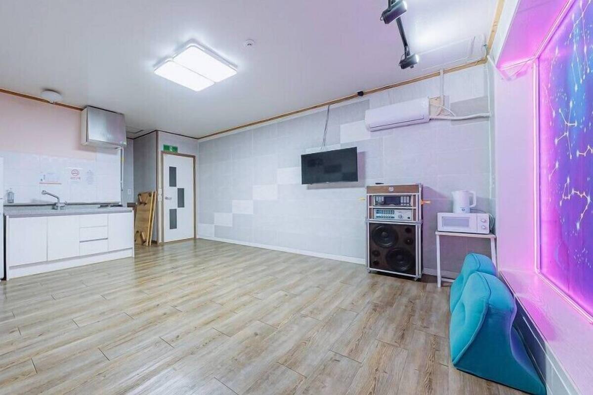 A spacious room with a kitchen area, a flat-screen TV mounted on the wall, and a neon light decoration.