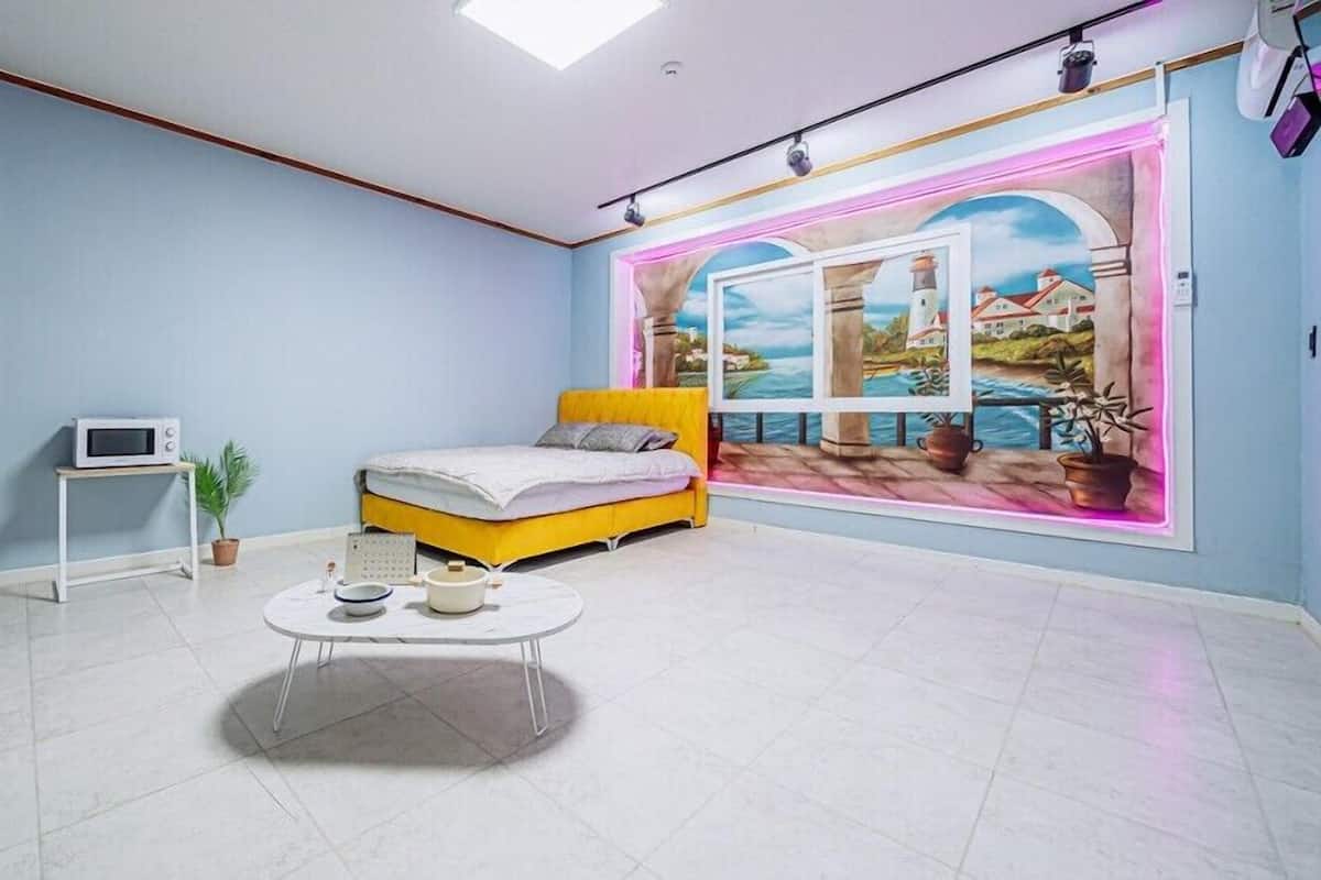 A bedroom with a bed, a small table, a microwave, and a potted plant.