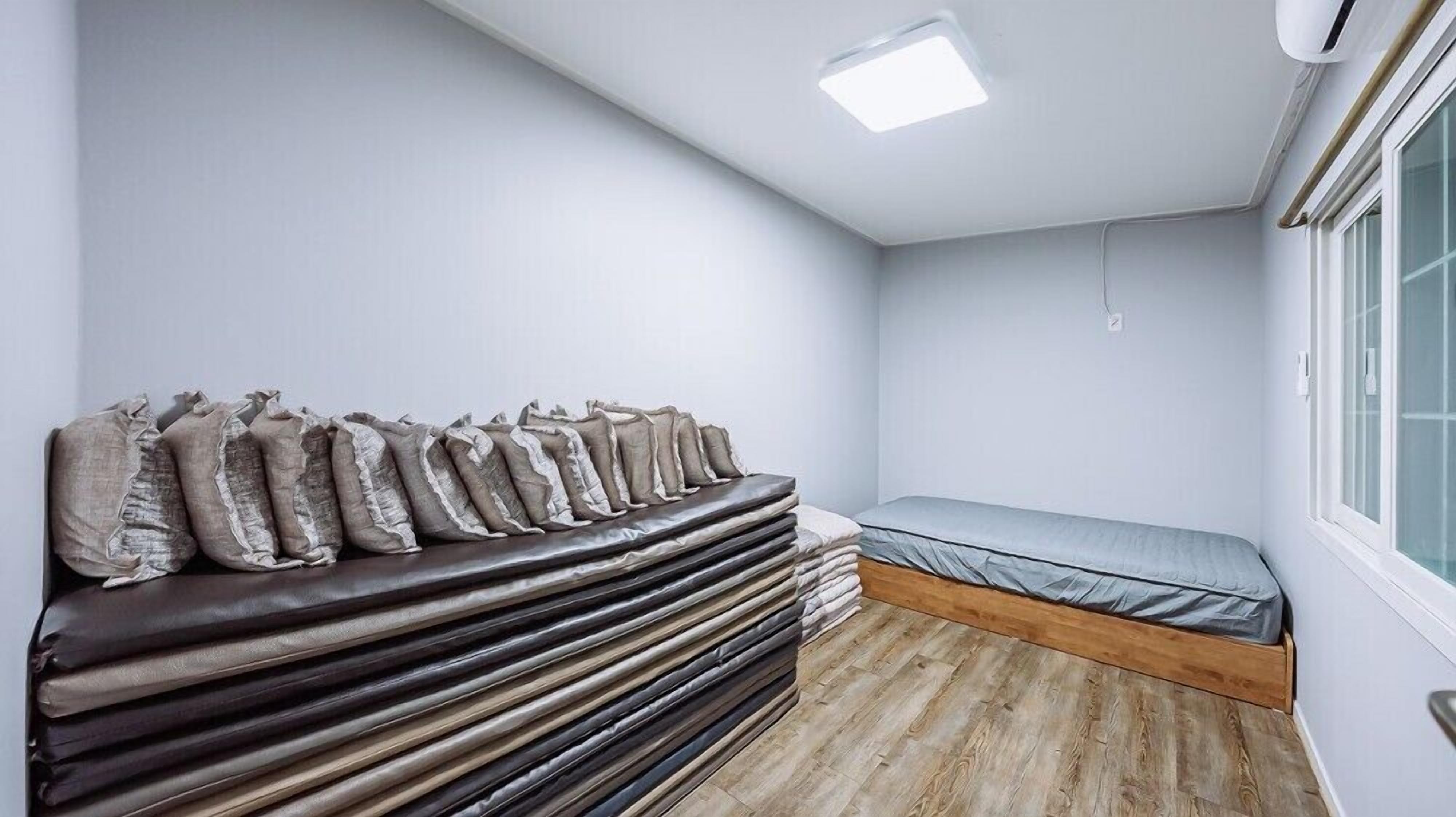 A small, compact room with a bed, a stack of mattresses, and a window.