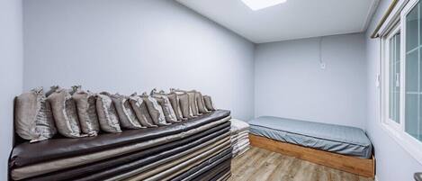 A small, compact room with a bed, a stack of mattresses, and a window.