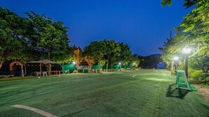 Ein Tennisplatz im Freien bei Dämmerung mit überdachter Sitzgelegenheit und Bäumen.
