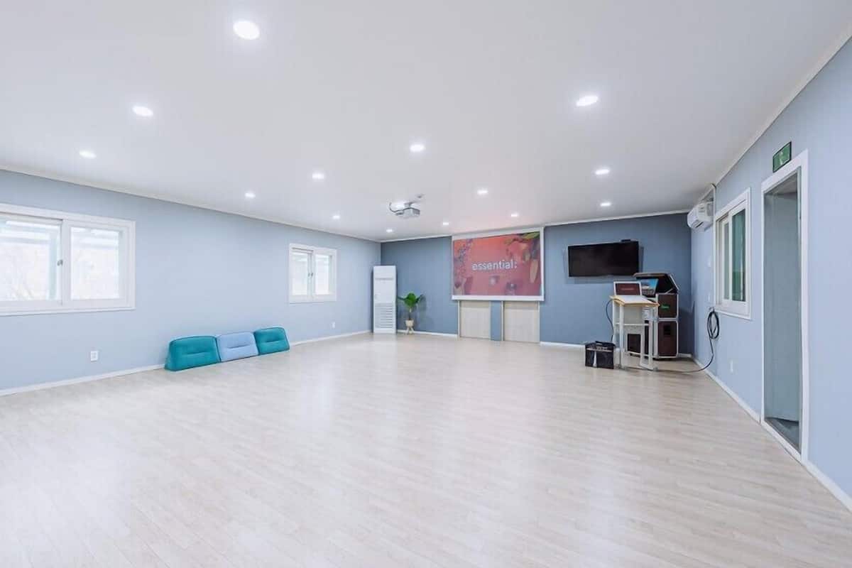 A spacious room with light wooden flooring, a large window, a wall-mounted TV, and a projection screen.