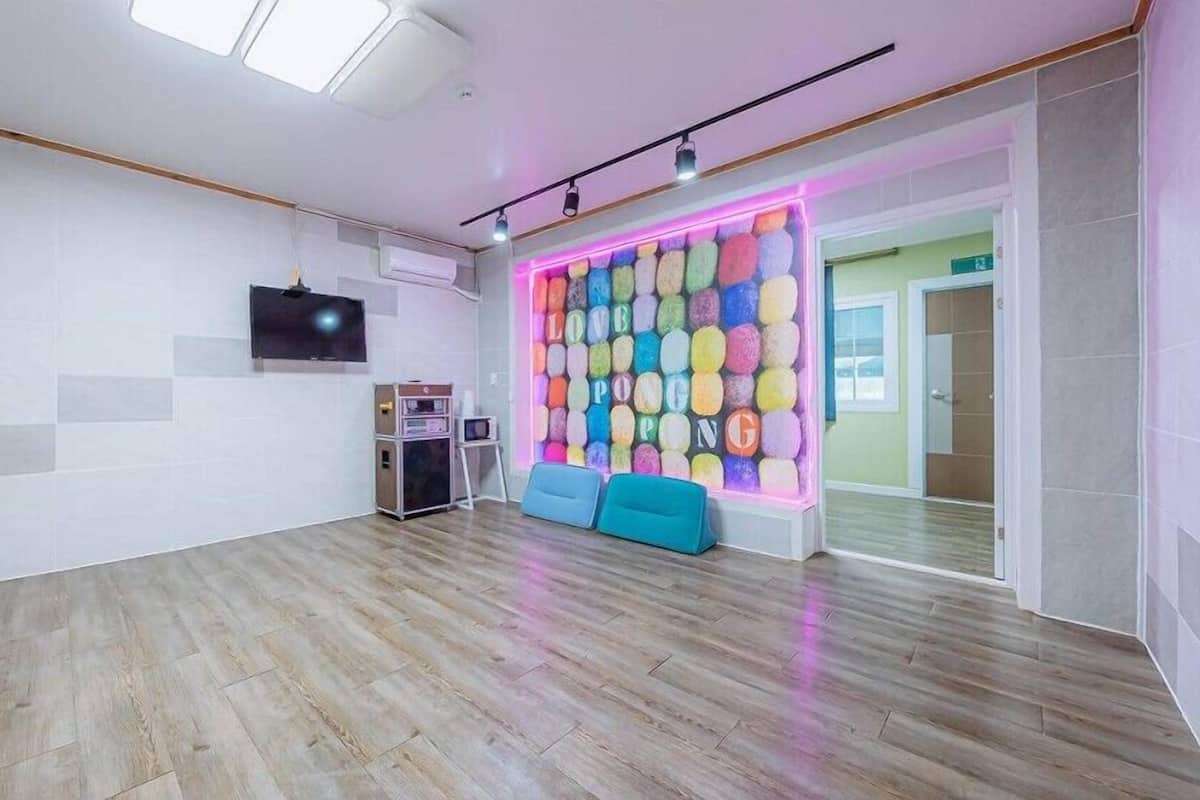 A spacious room with a wooden floor, a flat-screen TV mounted on the wall, and a colorful wall decoration.