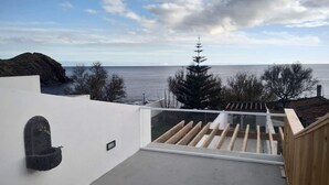 Une terrasse moderne sur le toit, offrant une vue sur la mer, agrémentée d’un élément décoratif en pierre et d’une clôture en bois.