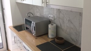 Une cuisine moderne avec des meubles blancs, un four à micro-ondes, une bouilloire et un plan de travail en bois.
