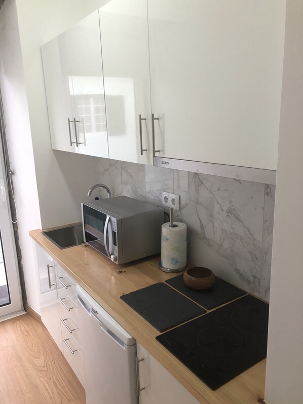 A modern kitchen with white cabinets, a microwave, a kettle, and a wooden countertop.