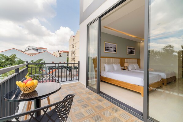 Un balcón con mesa y sillas, una cama con dos almohadas y una ventana con vistas a edificios.